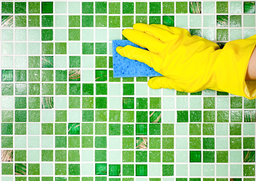 Yellow-gloved hand cleaning green tile to illustrate the Mini Mops House Cleaning article on the difference between Cleaning, Sanitizing, and Disinfecting